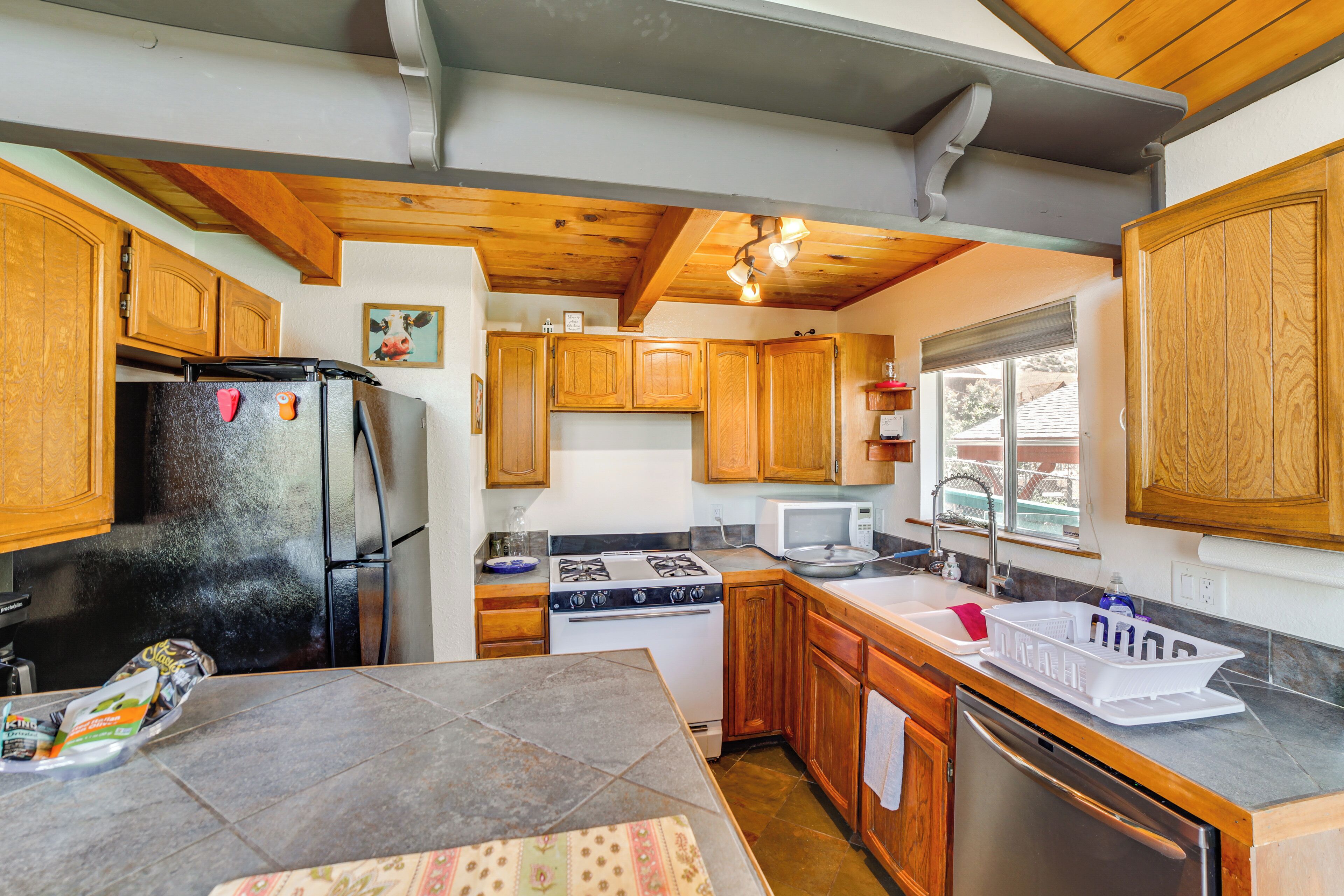 A compact kitchen with wooden cabinets, a refrigerator, stove, microwave, and dishwasher.