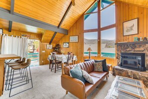 Interior acogedor de una cabaña con techo de madera, chimenea de piedra, sofá de cuero y comedor con mesa y sillas.