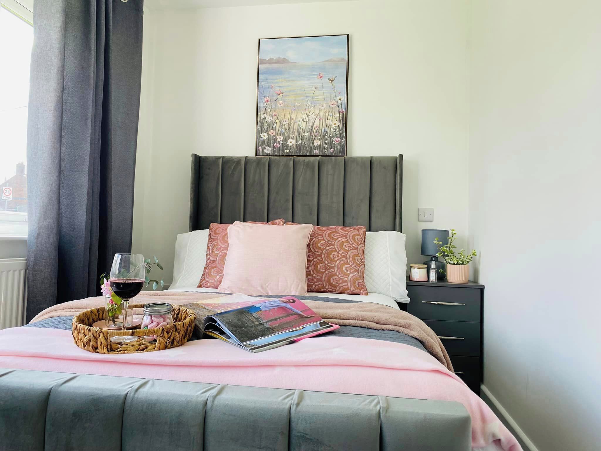 Un lit bien fait, avec un magazine, un verre de vin rouge et un panier contenant des bougies.