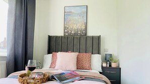 Una cama bien hecha con una revista, una copa de vino tinto y una cesta con velas.