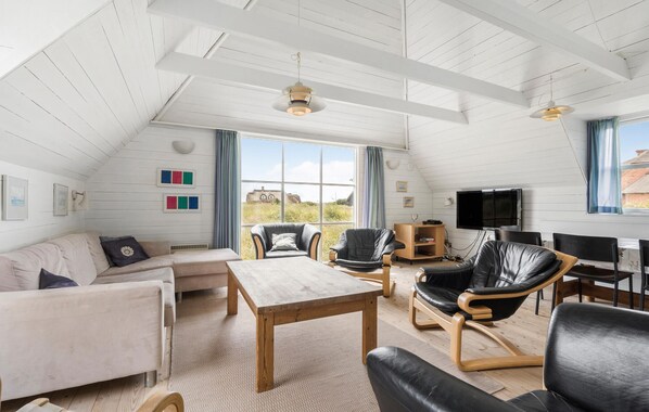 A spacious loft with a high ceiling, large windows, a wooden table, leather chairs, and a television.