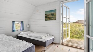 Een slaapkamer met twee bedden, een schilderij, een raam met gordijnen, en een open deur die uitkomt op een balkon.