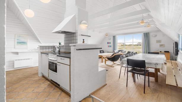 Een moderne keuken met witte kastjes, een inbouwoven en een eethoek met een houten tafel en stoelen.