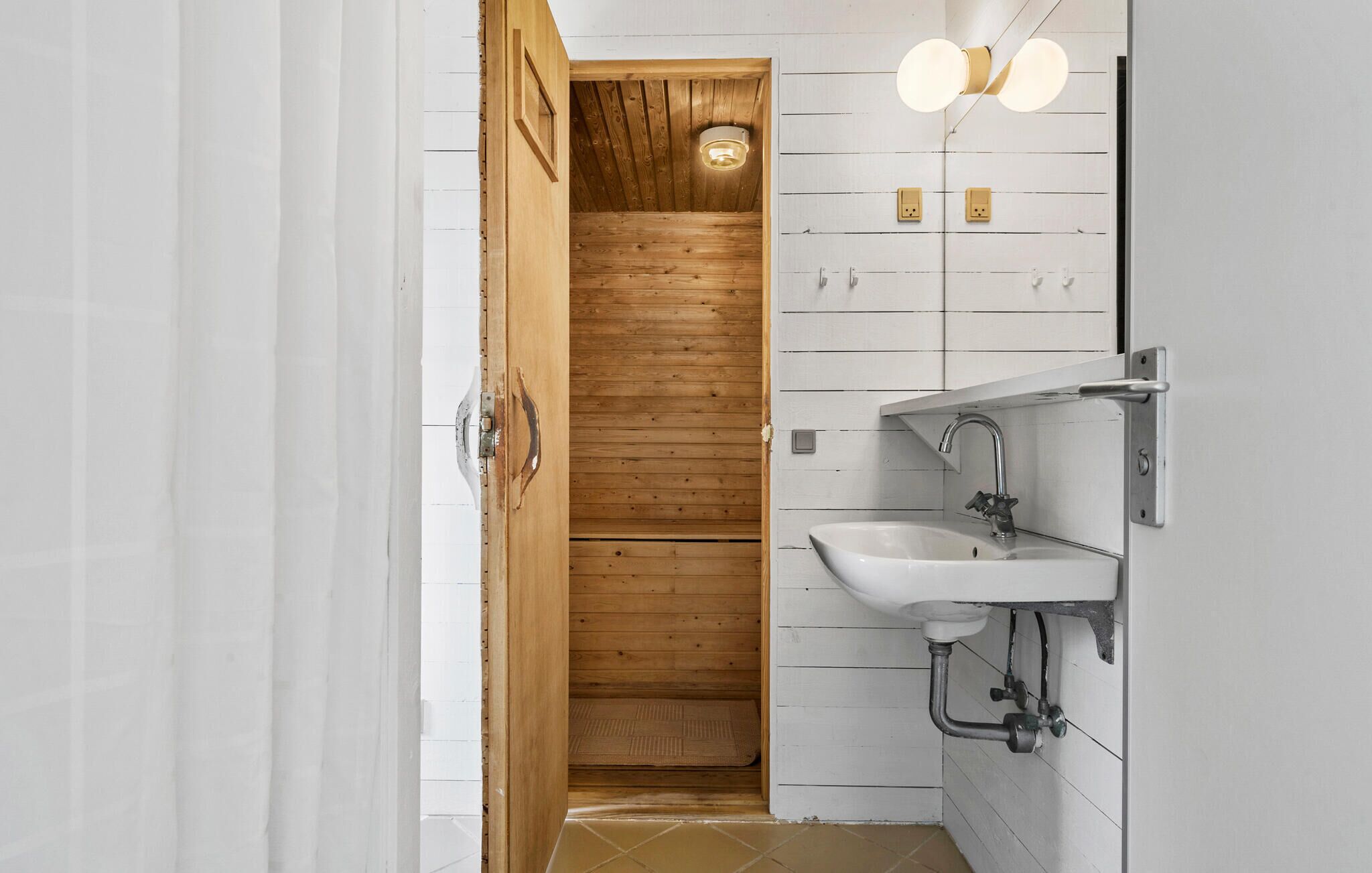 A bathroom with a wooden slatted wall, a white sink, and a mirror with two lights.