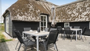 Een terras buiten met tafels en stoelen, een gebouw met rieten dak en een deur.