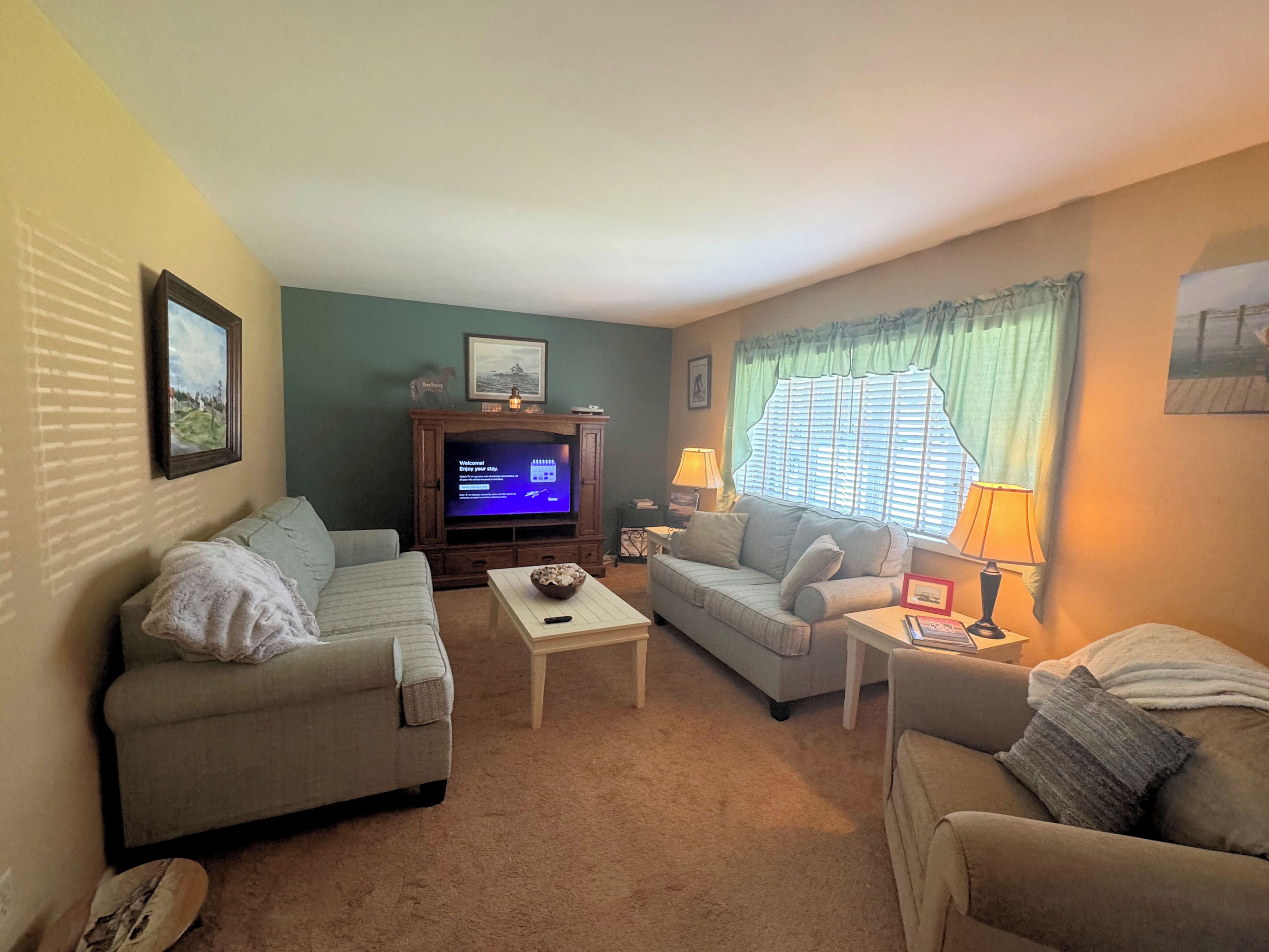 A living room with two sofas, a coffee table, a TV, and a window with curtains.