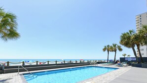Una piscina con vista sull'oceano, circondata da palme e lettini.
