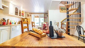 A wooden dining table with bread, a bottle, and a pitcher in a kitchen with white cabinets and a wooden staircase.