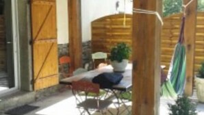 A covered patio area with a wooden table and chairs, a potted plant, and a hammock.
