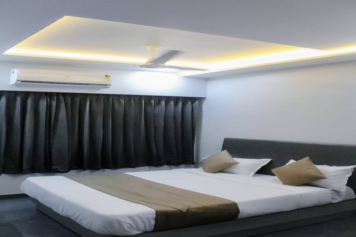 Una habitación de hotel moderna con cama, cortinas oscuras, ventilador de techo y aire acondicionado.