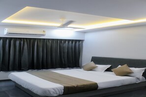 Una habitación de hotel moderna con cama, cortinas oscuras, ventilador de techo y aire acondicionado.