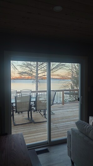 A room with a sliding glass door leading to an outdoor deck with a view of a lake and trees. - Waterfront Cottage | 3 bedroom | 1 bath | sleeps 6 people with Gourmet Kitchen (Arden)