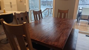 A dining area with a wooden table and chairs, a window with a view of a snowy landscape, and a kitchen area with cabinets and a countertop.