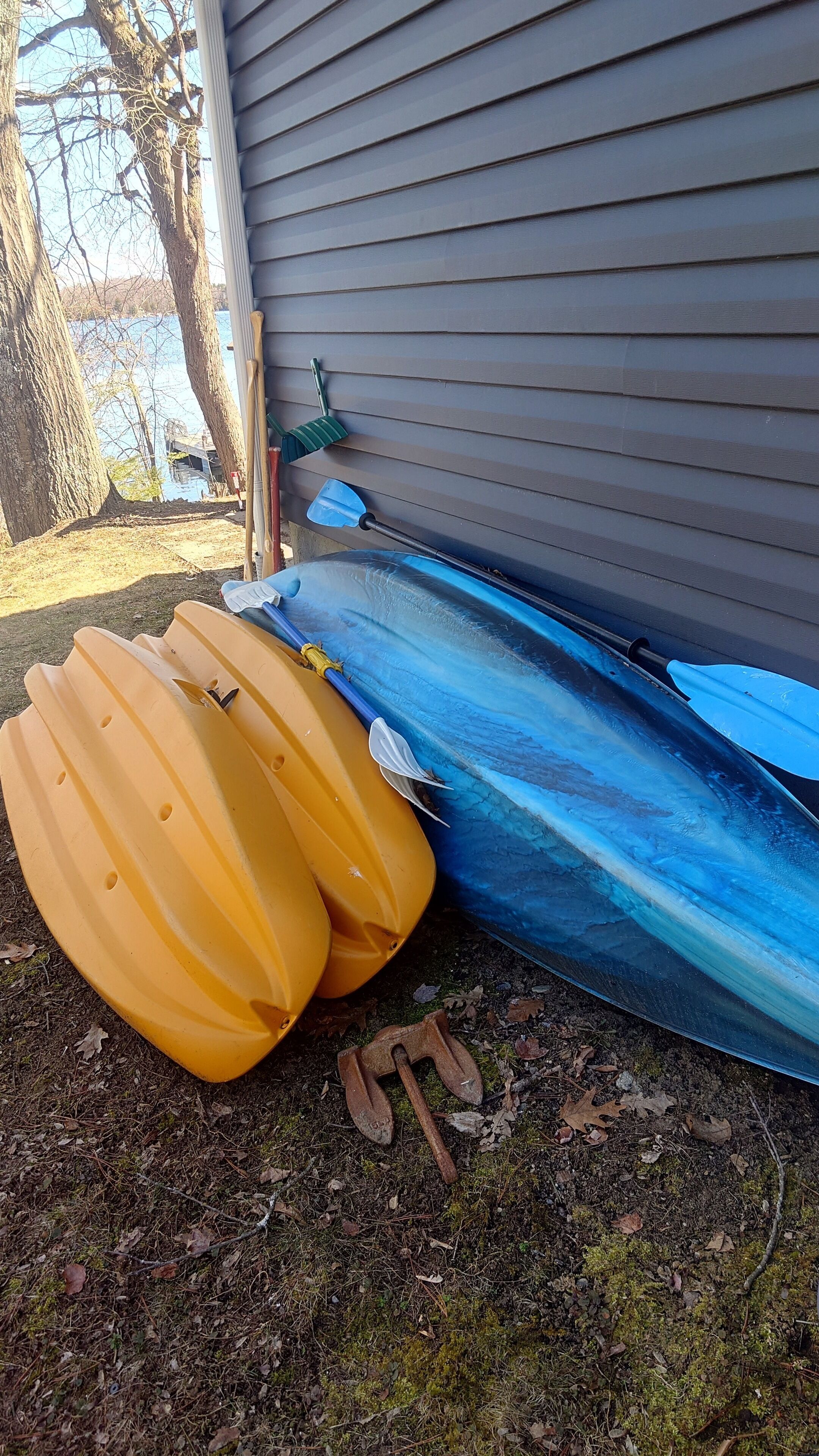 A kayak and paddle leaning against a house.