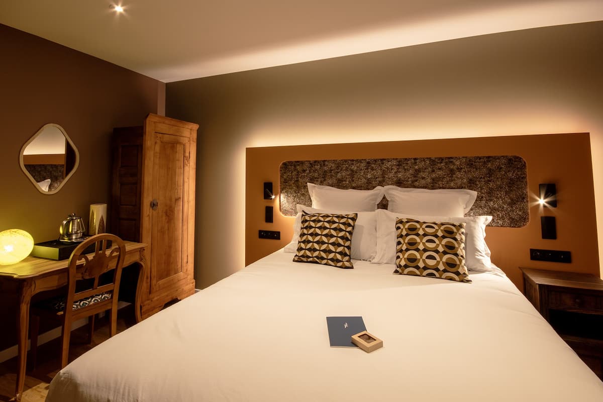 A neatly arranged hotel room with a large bed, a wooden desk, a chair, and a wardrobe.