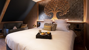 Un dormitorio moderno con una cama grande, un cuadro de pared con motivos de árbol decorativo, un sofá con cojines y una bandeja con alimentos para el desayuno.