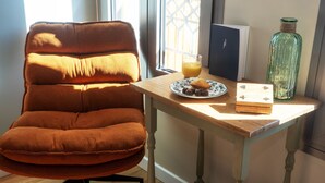 Una habitación acogedora con un sill ón naranja mullido, una mesa de madera con un plato de comida y un vaso de jugo de naranja, y una botella verde.