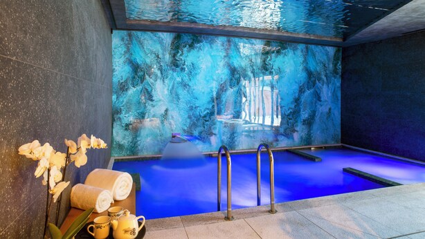 Un área de spa con una piscina iluminada en azul, un juego de toallas y té, y orquídeas.