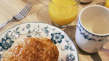 A breakfast table with a pastry, a glass of orange juice, a mug, and a jar of jam.