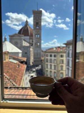 A hand holding a cup of coffee with a view of a historic building and a tower in the background. - Casa Luisa: Your home in the heart of Florence with breathtaking views. (Firenze)