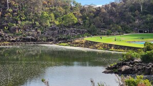 A serene lakeside view with a golf course and rocky terrain.