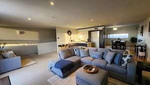 A modern living room with a sectional sofa, a small ottoman, and a dining area with a table and chairs.