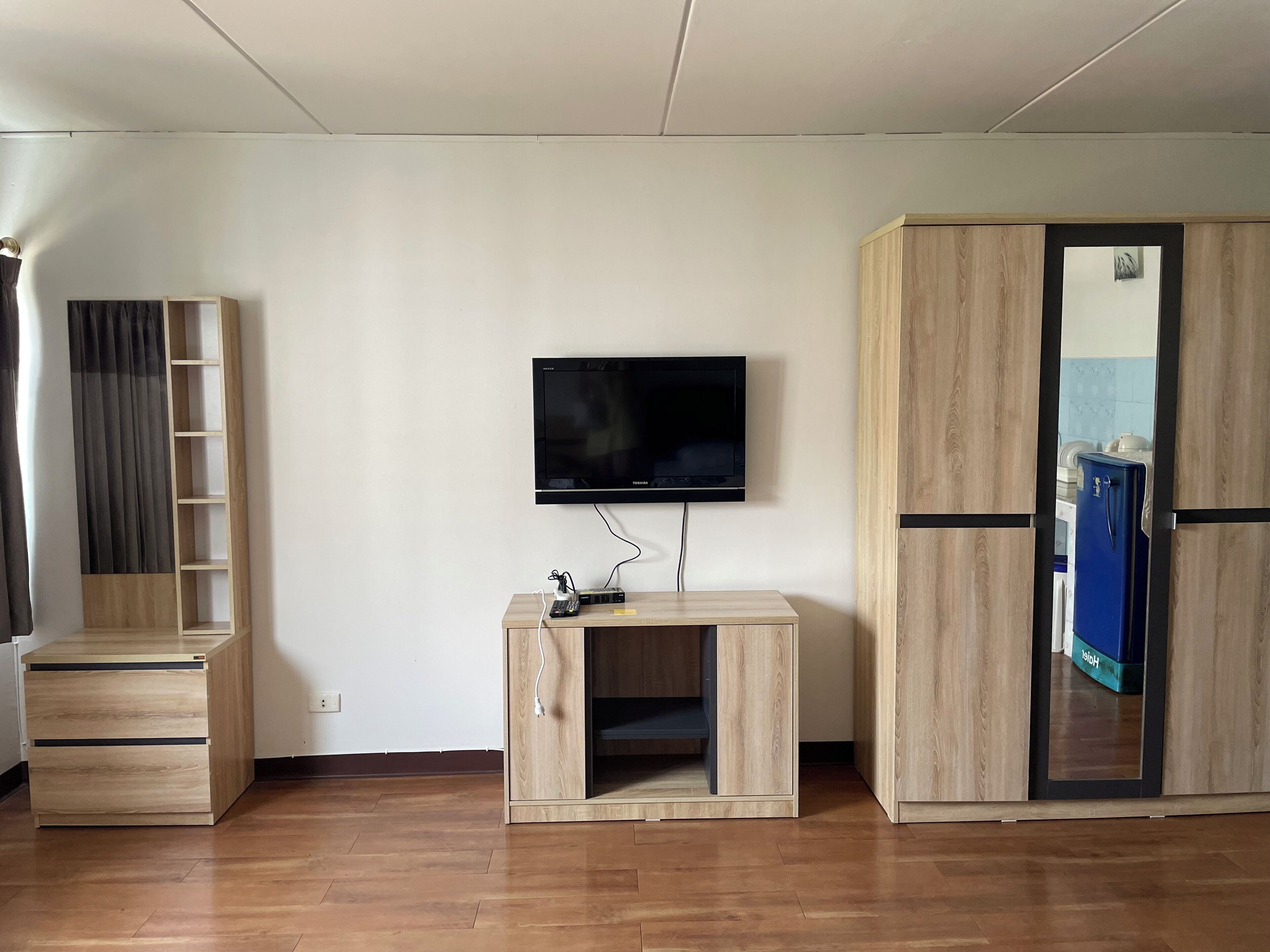 A room with a flat-screen TV mounted on the wall, a wooden cabinet with a mirror, and a blue refrigerator.