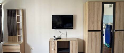 A room with a flat-screen TV mounted on the wall, a wooden cabinet with a mirror, and a blue refrigerator.