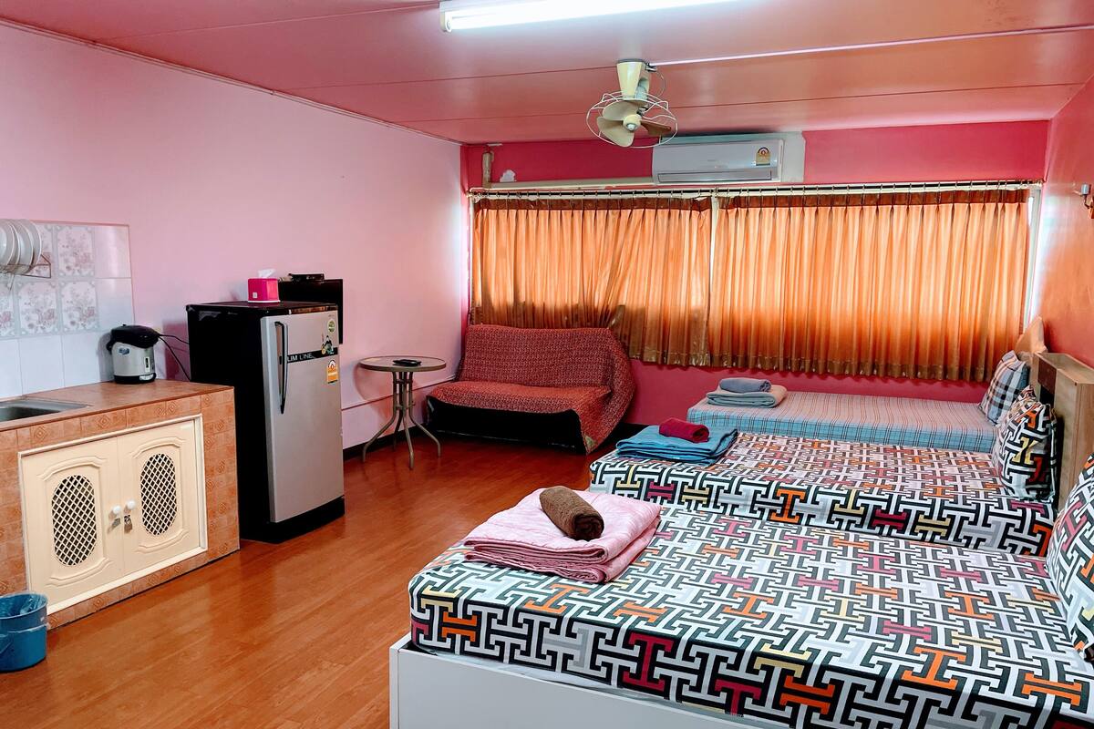 Una habitación pequeña con cama, una mesita, un refrigerador y una ventana con cortinas.