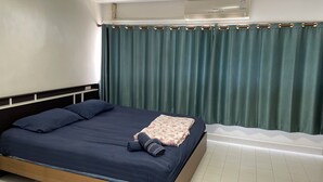 A single bed with a dark blue mattress and pillows, a floral-patterned blanket, and a rolled-up towel. - Impact Muangthong C1-C9 by Anna (Pak Kret)