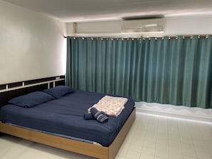 Una cama individual con un colchón y almohadas azul oscuro, una colcha estampada con motivos florales y una toalla enrollada.