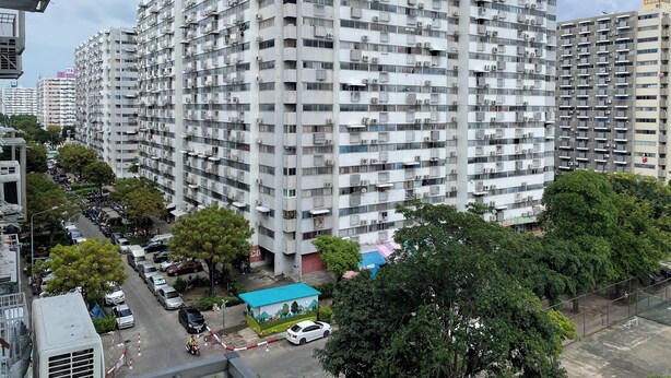 A high-rise residential building with multiple balconies, a parking area, and surrounding greenery. - Impact Muangthong C1-C9 by Anna (Pak Kret)