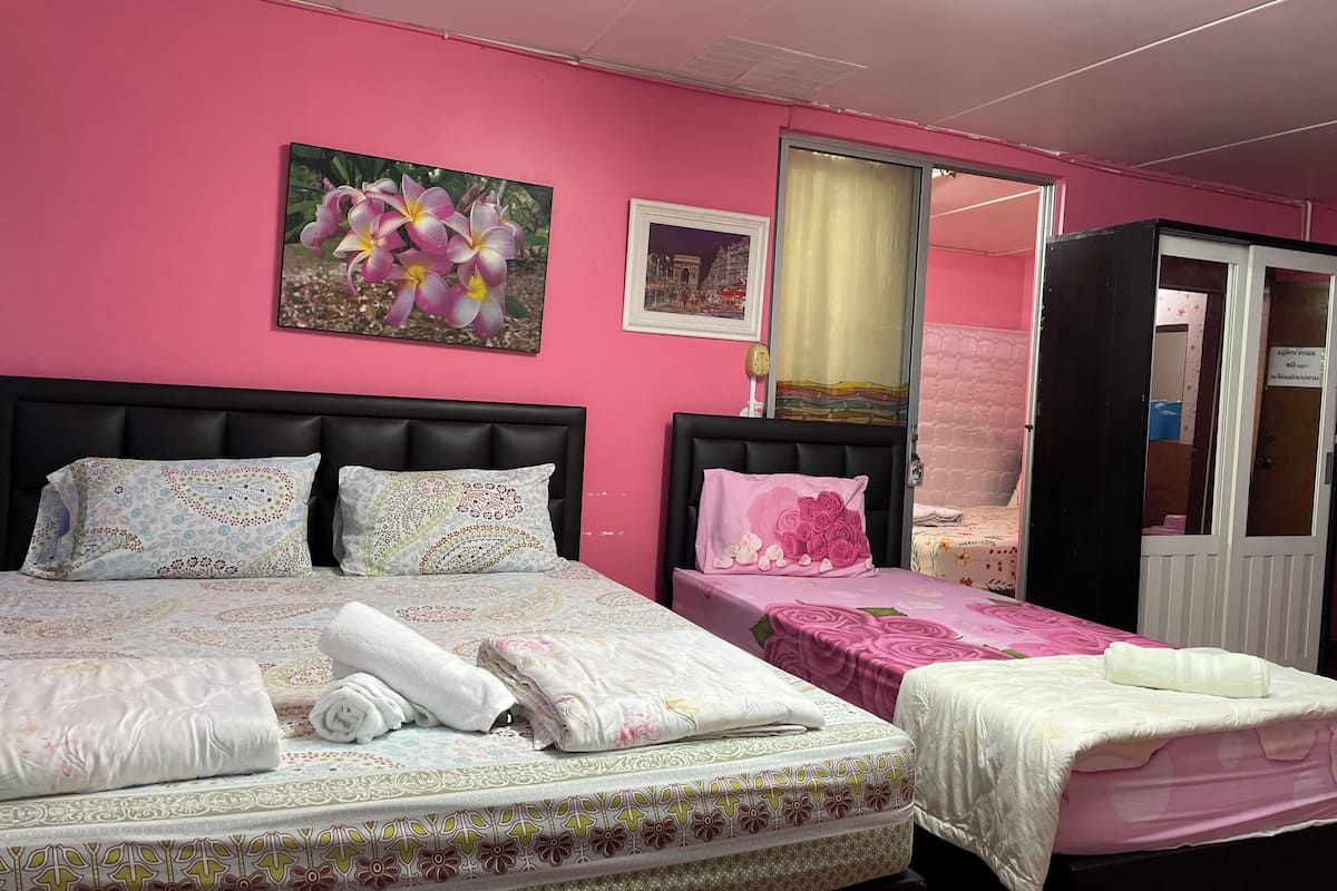Una habitación con dos camas, una pared rosa y una puerta que da a otra habitación.