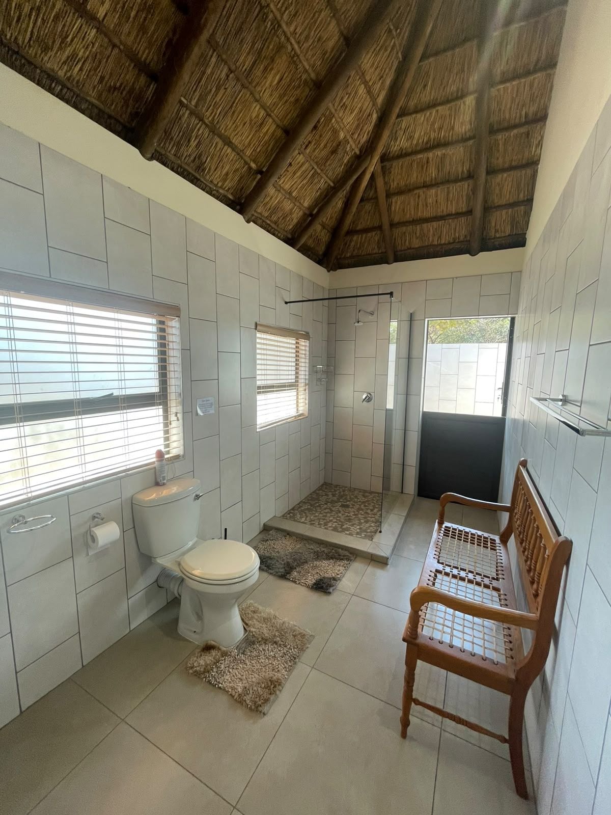 A bathroom with a toilet, shower, and a bench.