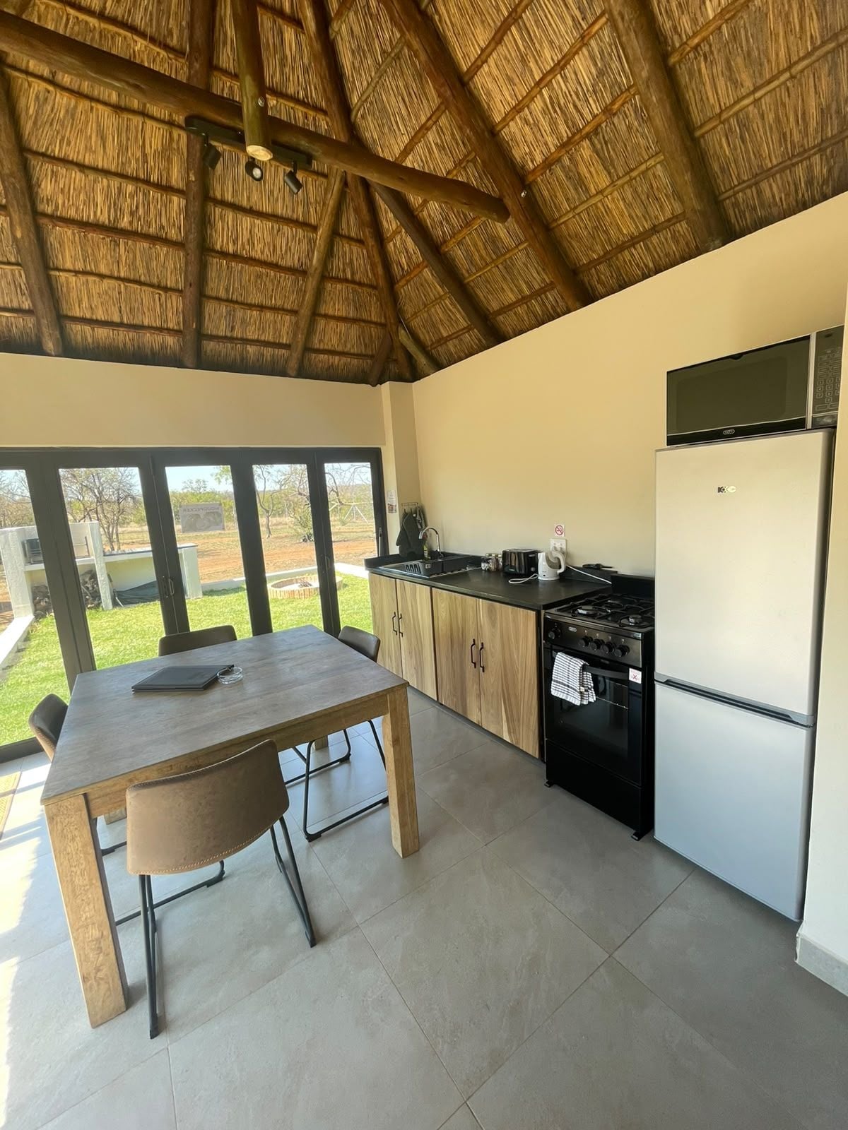 A kitchen with a thatched roof, a dining table with chairs, a stove, and a refrigerator.