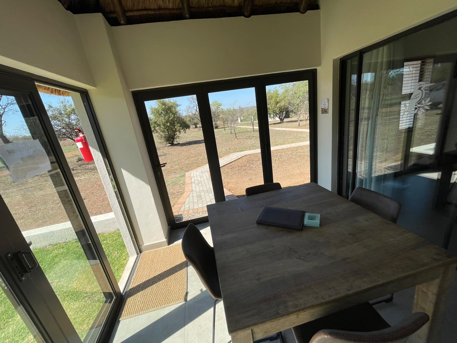 A room with a wooden table and chairs, large windows, and a view of a landscaped outdoor area.