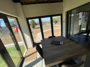 Una habitación con una mesa y sillas de madera, ventanas amplias y vistas a un área exterior ajardinada.