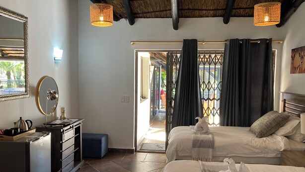 A hotel room with two beds, a desk with a kettle, a mirror, and a ceiling fan.