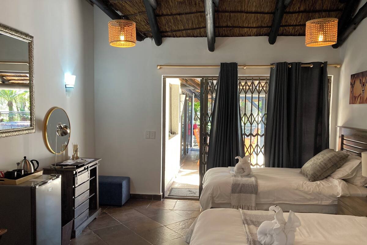 Une chambre d’hôtel avec deux lits, un bureau avec une bouilloire, un miroir et un ventilateur de plafond.