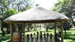 A gazebo with a thatched roof, chess pieces arranged on a platform, and a large wooden barrel.