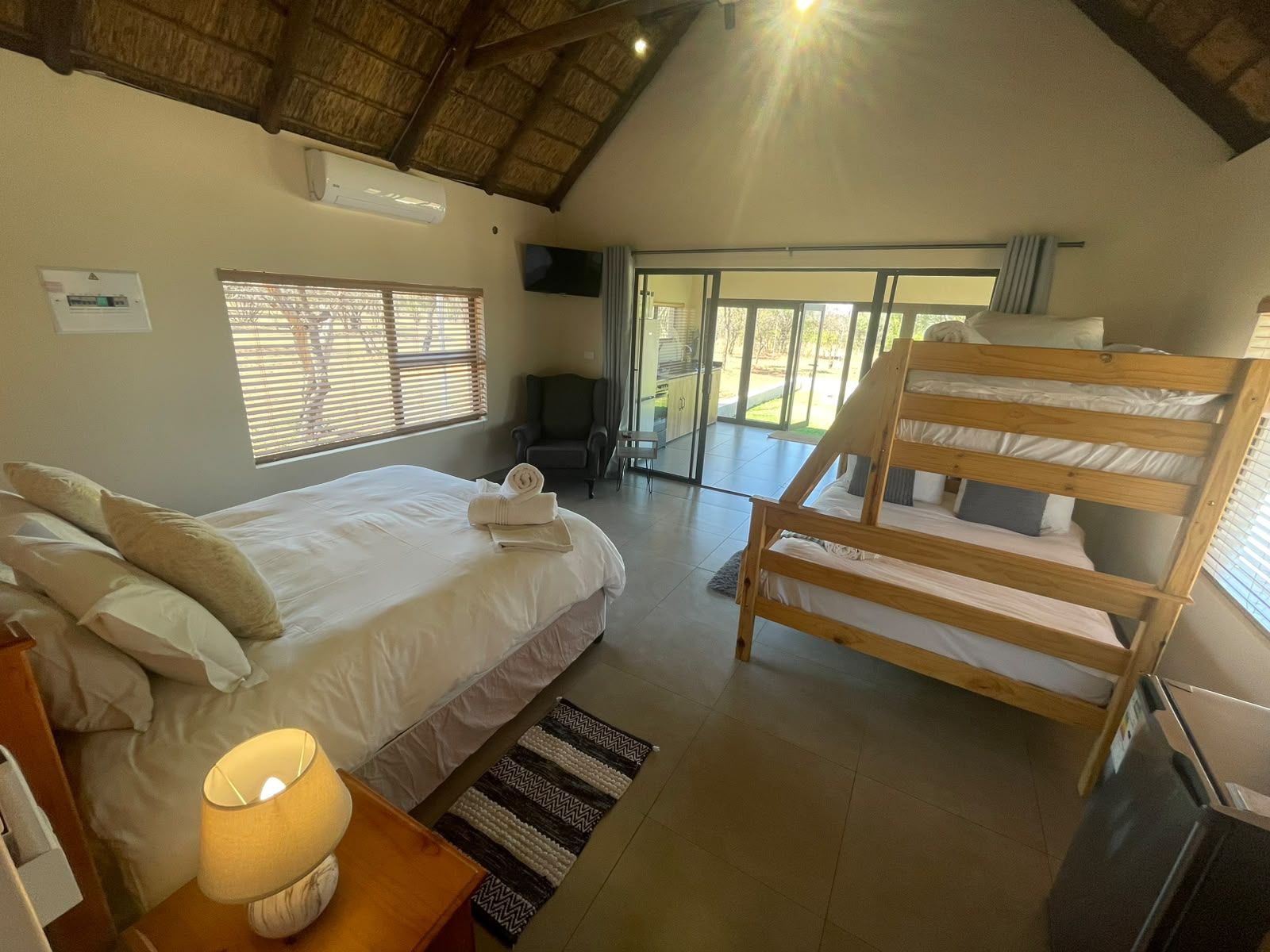 A bedroom with a bed, a chair, a desk, a TV, and a window.