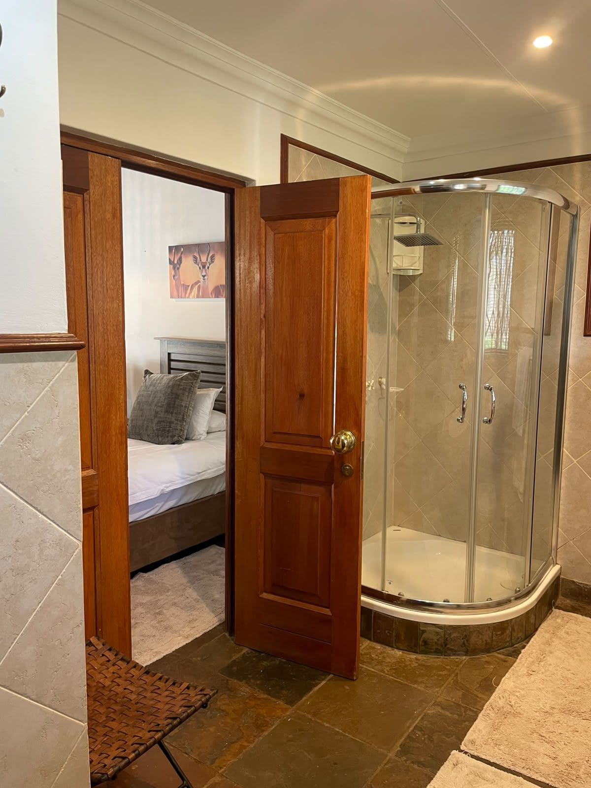 A bathroom with a shower, a wooden door, and a bed with pillows.