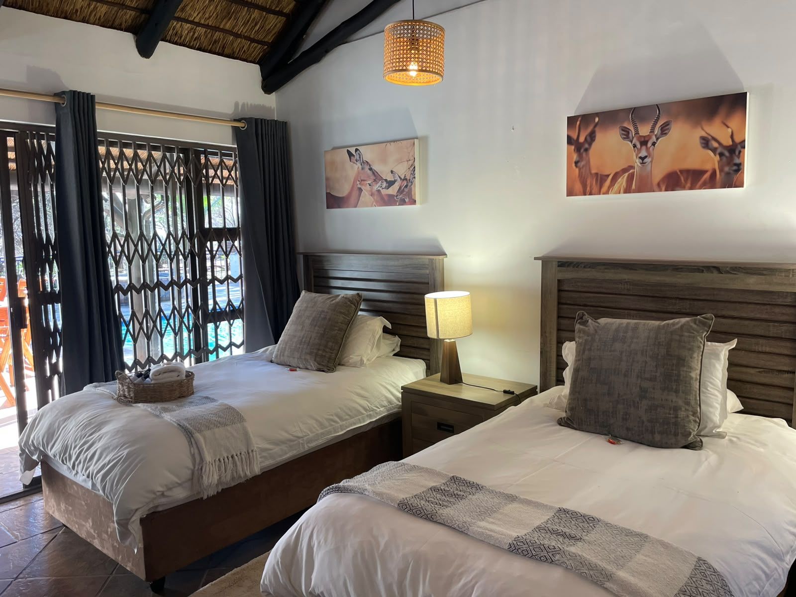 A hotel room with two beds, a nightstand with a lamp, and artwork on the walls.