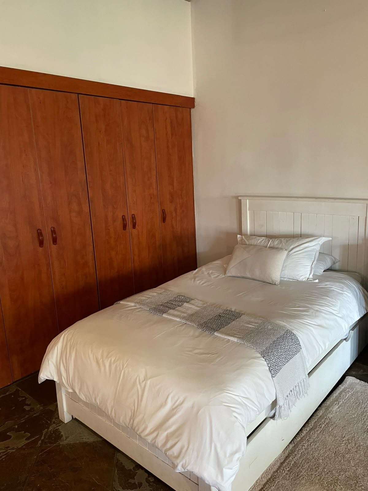 Ein Schlafzimmer mit einem Bett, einem Holzschrank und einem weißen Kopfteil.
