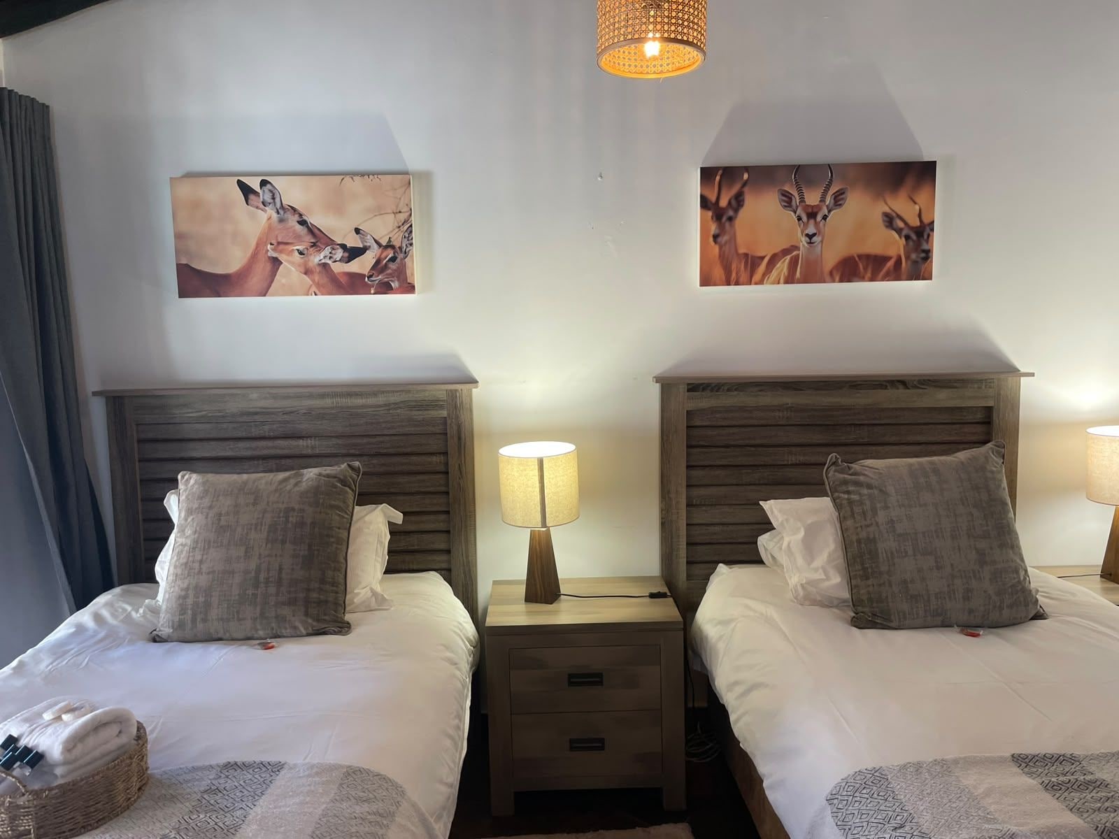 Quarto duplo com duas camas, cada uma com cabeceira de madeira, mesa de cabeceira e luminária. Há duas obras de arte na parede retratando animais.