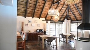 A spacious kitchen with a high ceiling, a dining area with wooden furniture, and a large window allowing natural light.