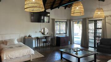 A room with a bed, desk, and seating area, featuring a TV, wicker lamps, and a glass coffee table.