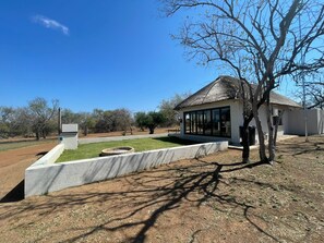 A modern building with a thatched roof, a covered outdoor seating area, and a landscaped garden with a circular stone feature.