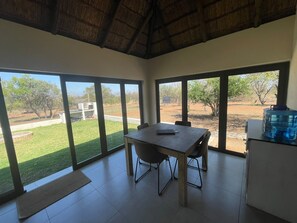 A room with a dining table and chairs, large windows with a view of a grassy area and trees, and a water dispenser on a cabinet.