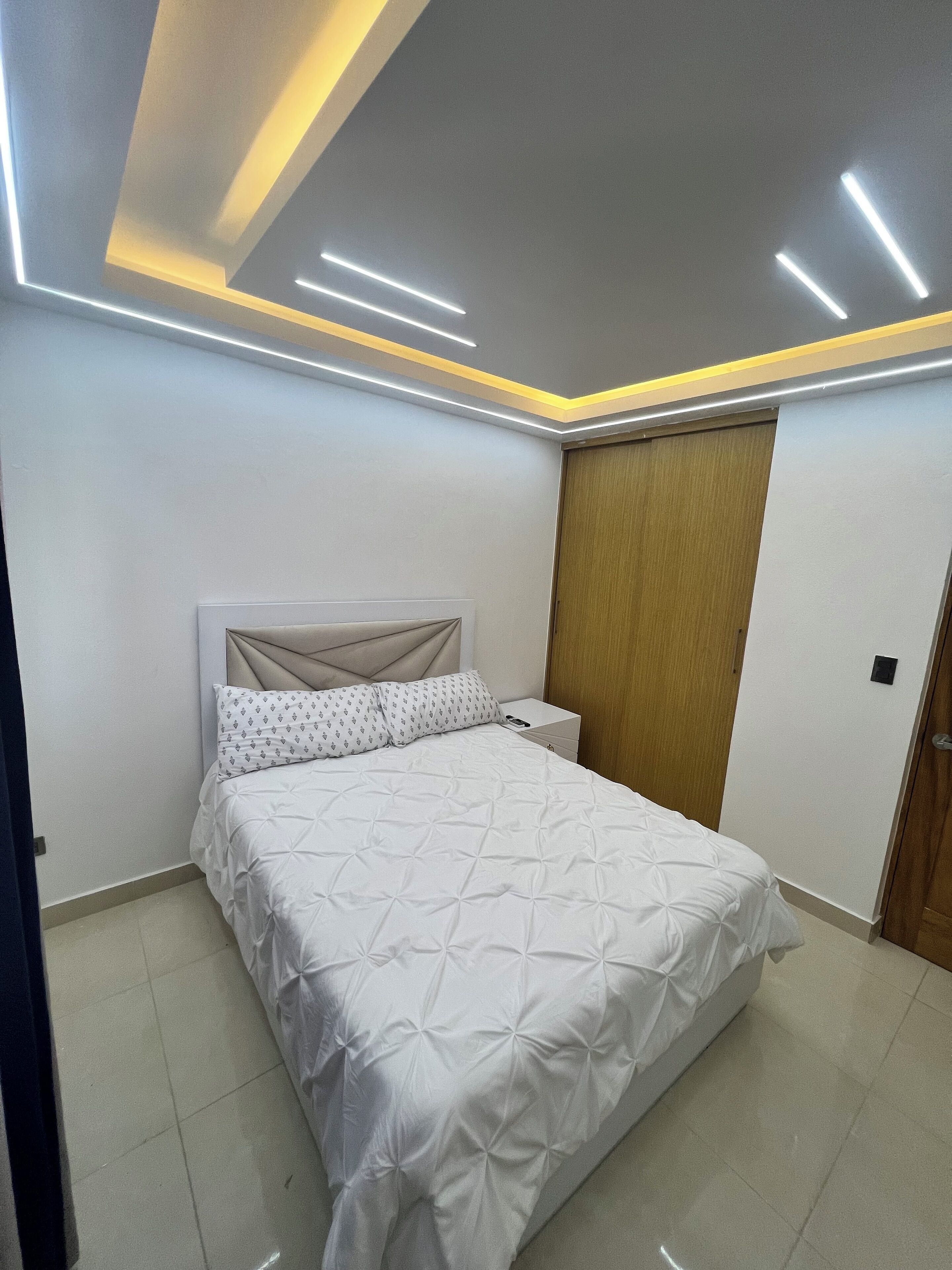 A modern bedroom with a bed, a nightstand, and a wooden wardrobe.
